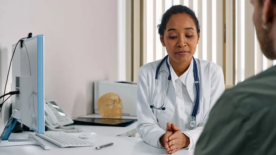 Dermatologist consulting with a patient at a clinic desk with a laptop
