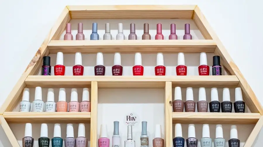 Wall display of colour-sorted nail polish bottles on wooden shelves in a salon