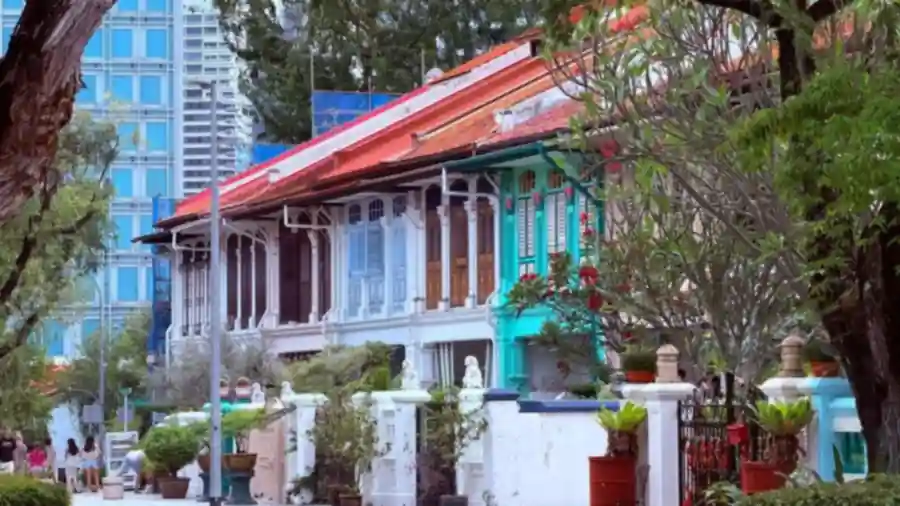 Row of colourful two-storey shophouses on a Malaysian suburban street with high-rise blocks behind