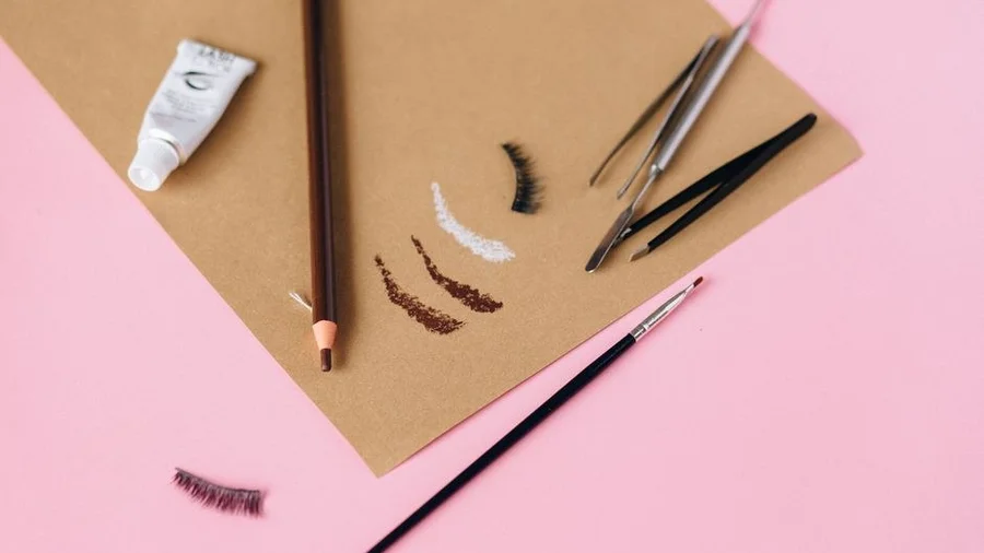 Flat lay of eyebrow shaping tools including tweezers, brush and pencil