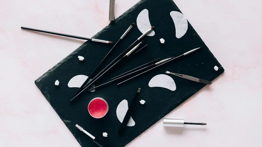 Flat lay of lash and brow beauty tools on a dark tray