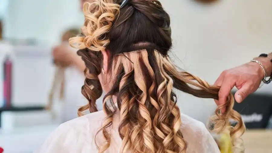Hairstylist installing curled hair extensions, back view