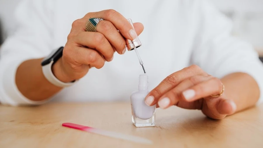 Person applying gel polish at home with a bottle on the table
