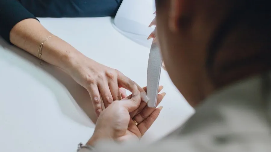 Manicurist filing a client's nails at a salon table