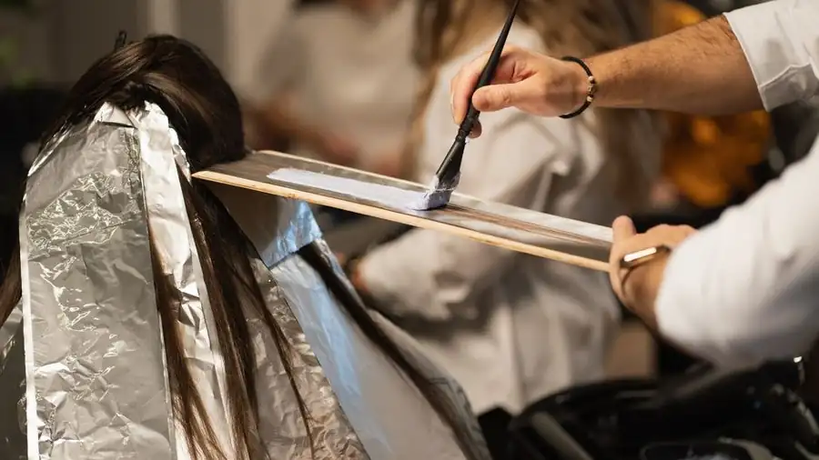 Stylist applying colour to sectioned hair with foils and a tint brush