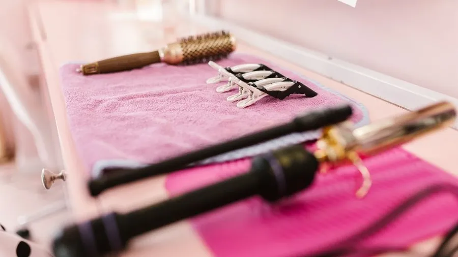 Curling iron, round brush and sectioning clips laid out on a salon towel