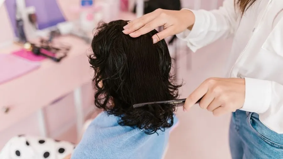 Stylist sectioning a client's dark wavy hair at a salon station
