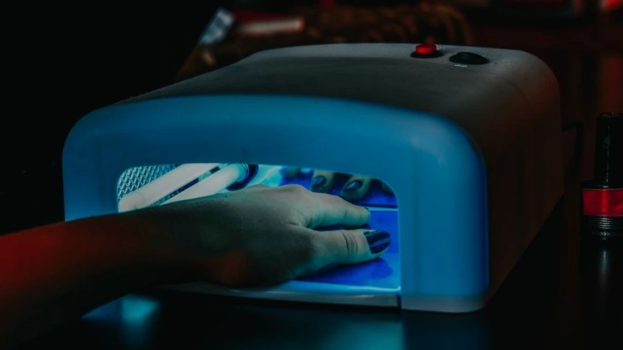 Hand with manicured nails curing under a blue LED nail lamp