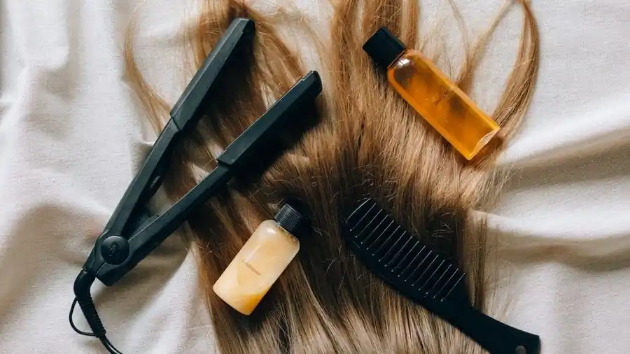 Flat lay of a hair straightening iron, comb and treatment product bottles