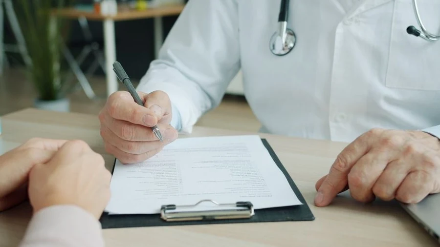 Doctor's hands writing notes on a clipboard during a consultation