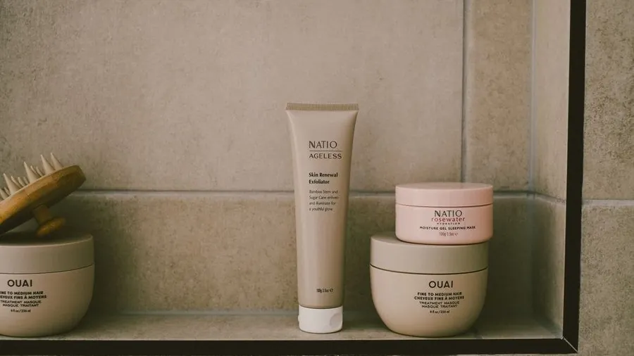 Skincare tubes and jars on a tiled bathroom shelf
