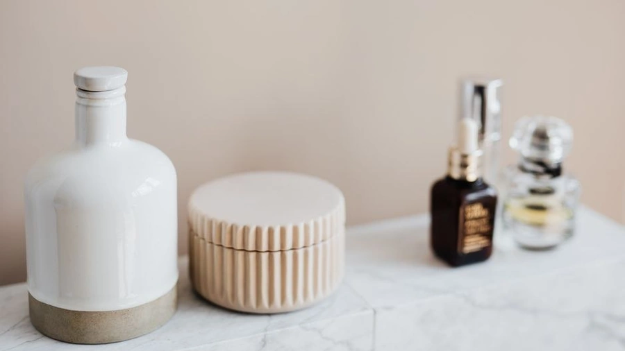 Cream jar and serum bottle on a pale marble shelf