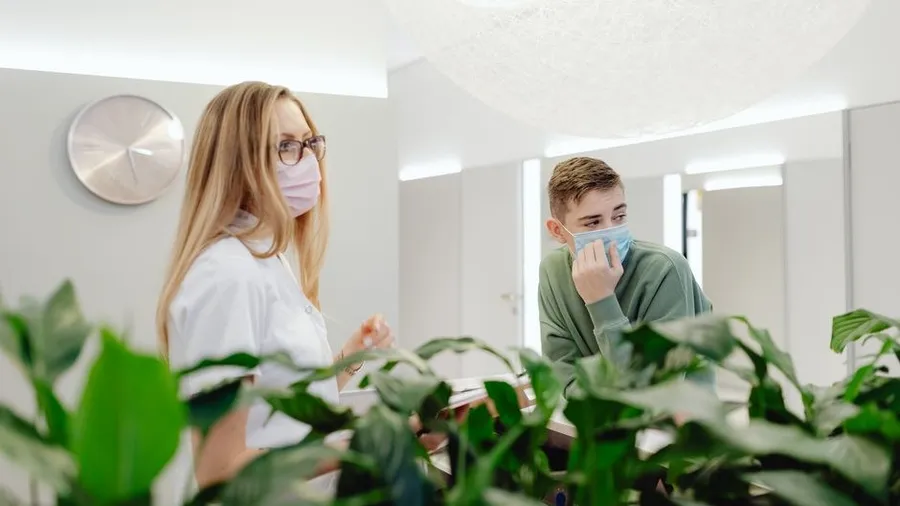 Bright clinic waiting area with two staff members among indoor plants