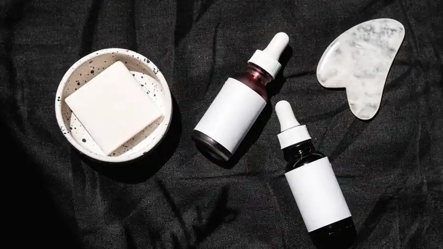 Flat lay of skincare serum bottles and a gua sha tool on dark fabric