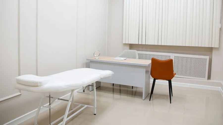 Minimalist clinic treatment room with a bed, desk and chair