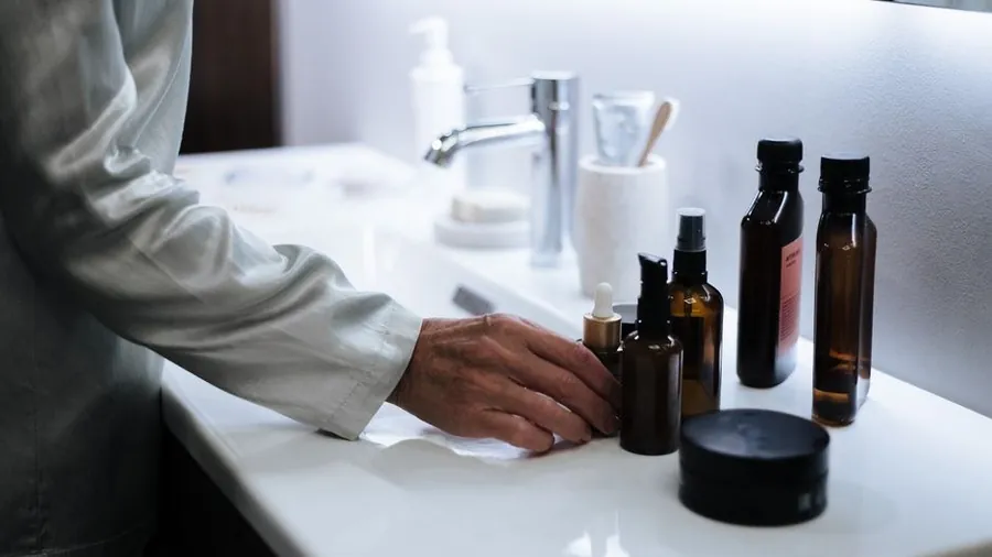 Hand reaching for amber skincare bottles arranged on a bathroom counter