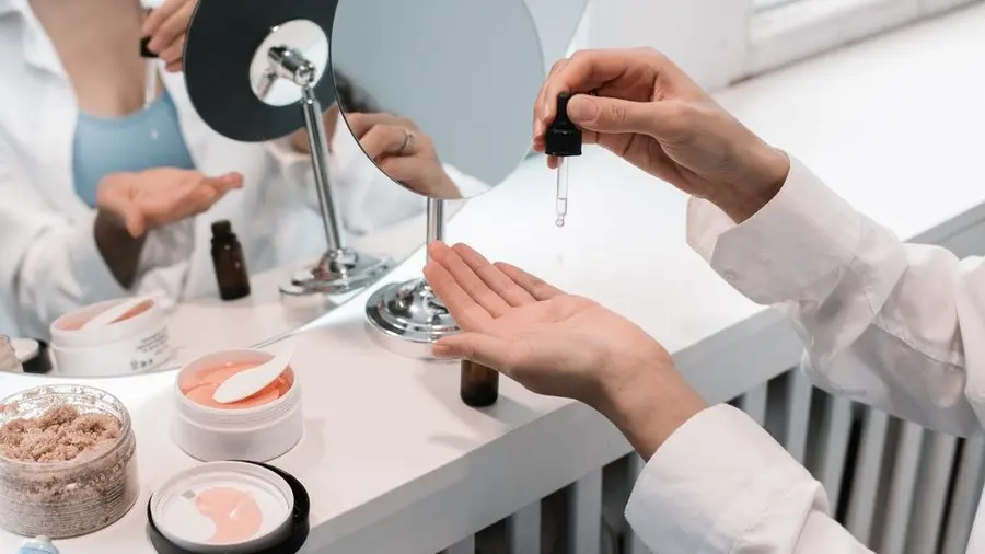 Hands arranging skincare bottles and dropper on a counter