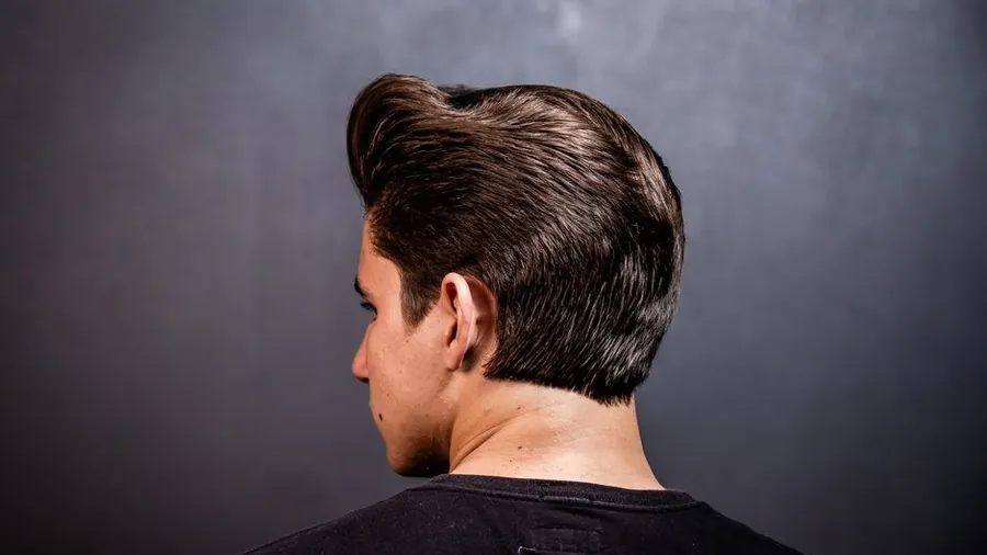 Back view of a man with short styled hair against a dark studio background