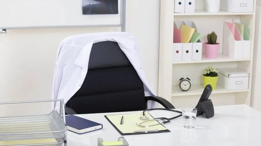 Empty consultation office desk with a doctor's white coat in a private clinic