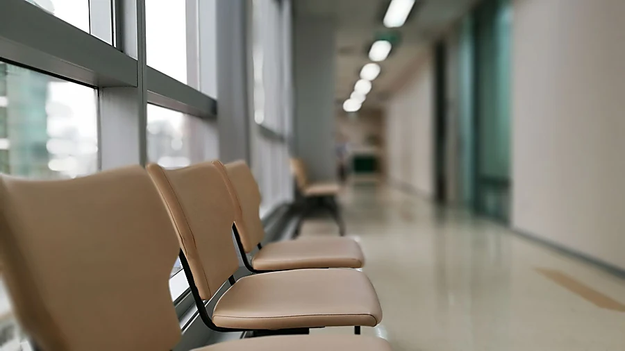 Empty clinic waiting area with a row of chairs along a bright corridor