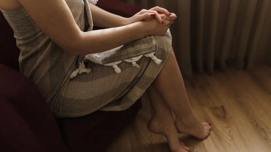 Woman sitting with hands folded in a wood-floored room