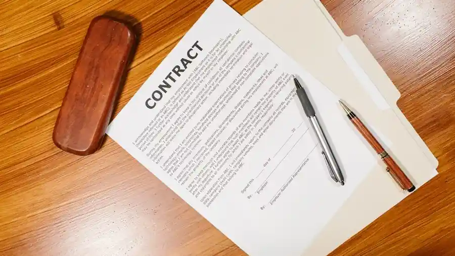 A printed contract document with two pens resting on a wooden desk
